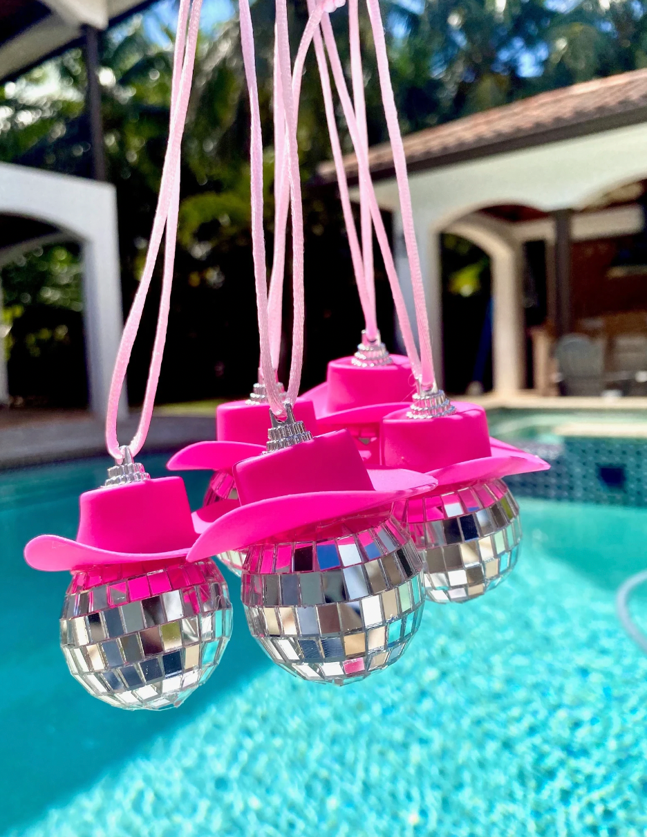 Small disco balls adorned with pink cowboy hats hanging on a string 
