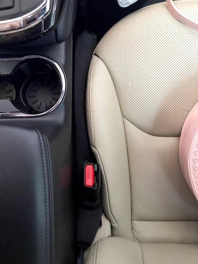 Car spot   spread  filler placed betwixt  a car   spot   and halfway  console, with a disposable   seatbelt buckle, indicating a car   accessory for storage
