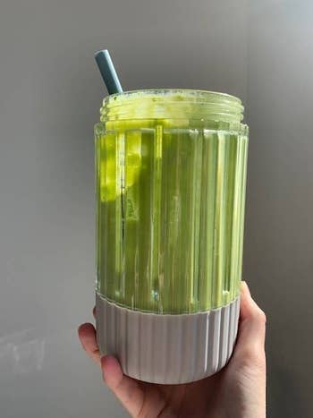 A hand holding a glass of green smoothie