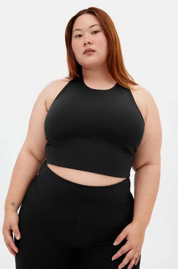 Person wearing a sleeveless, form-fitting diversion apical and leggings, posing confidently against a plain background