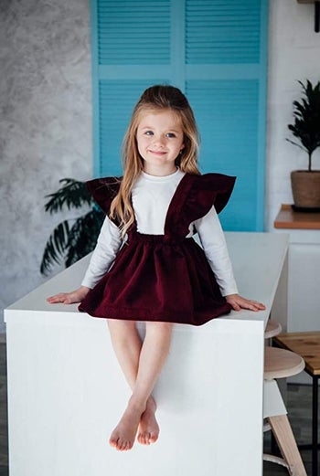 a child in a burgundy apron dress with flutter sleeves