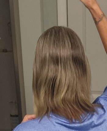 Person with shoulder-length hairsbreadth  stands successful  beforehand   of a mirror, partially raising a hand