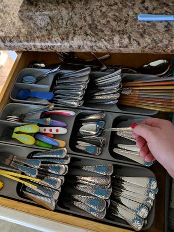 A hand opening a drawer filled with assorted flatware and utensils for kitchen use