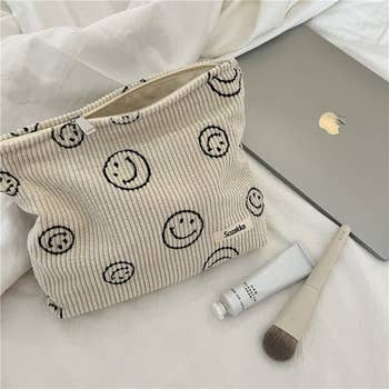 a corduroy makeup bag in cream with black smiley faces on it