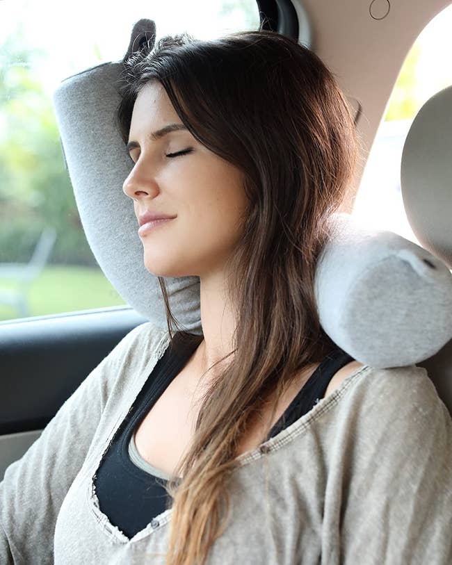 a model using the gray twist travel pillow to sleep in a car
