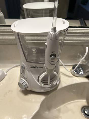 Countertop h2o flosser with power settings and h2o reservoir beside a sink