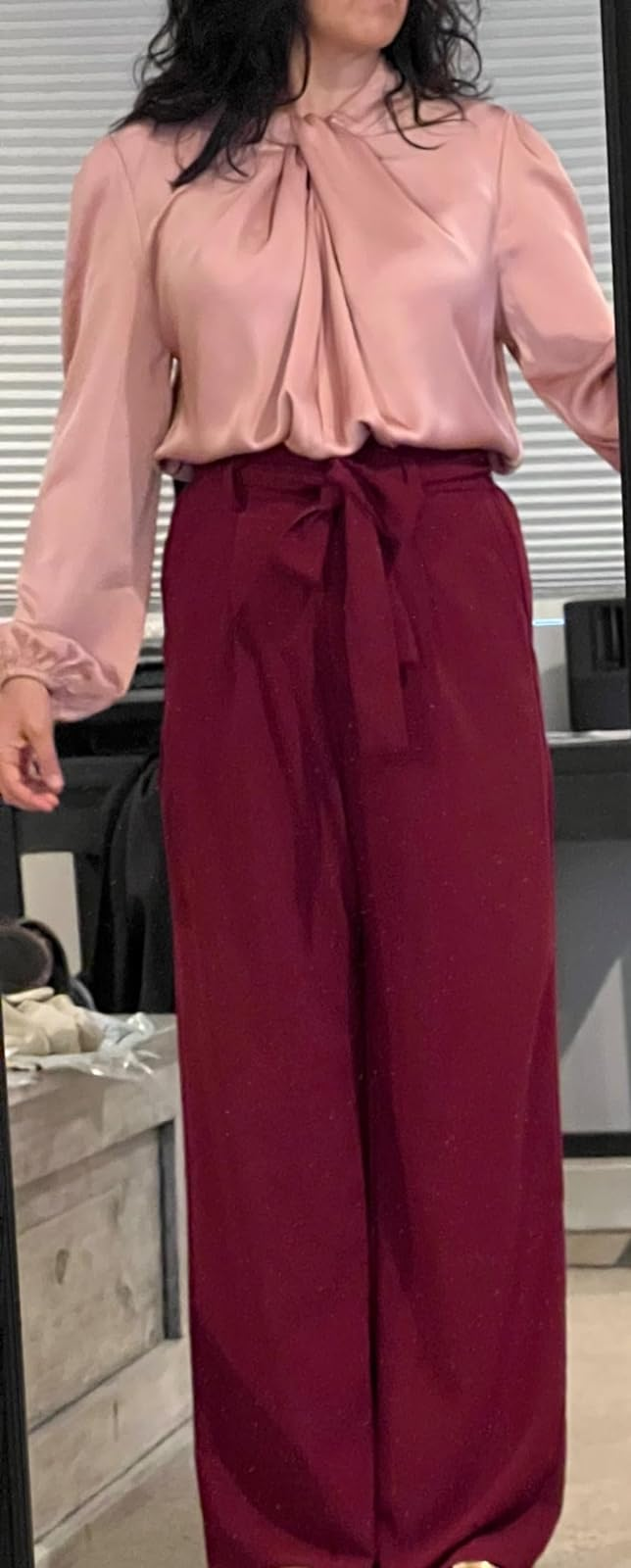 Person wearing a tie-neck blouse and high-waisted trousers