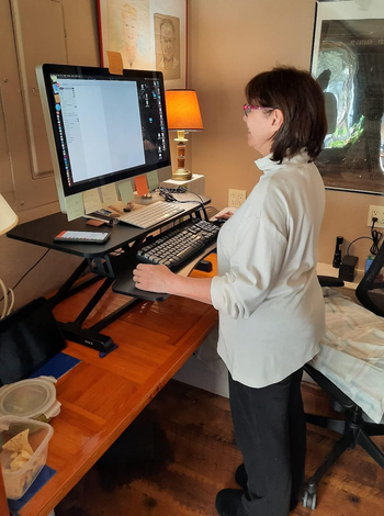 reviewer standing while using the sit-to-stand desk converter on top of their existing desk