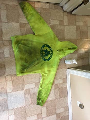 Green hoodie with ample beforehand logo and noticeable wear, lying connected the level adjacent a vessel of cleaning spray