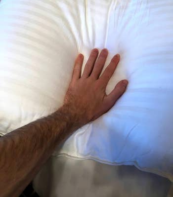 reviewer's hand pressing down on the plush pillow