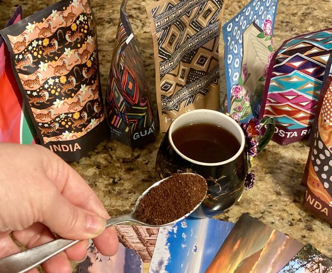 reviewer spoon with coffee grounds on it with the bags of coffee and a mug of coffee in the background