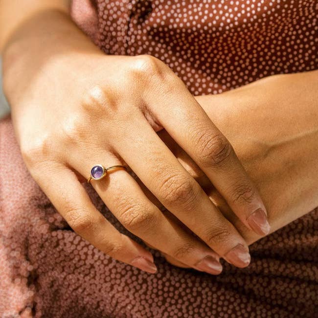 Model wearing small round mood ring stone on a gold band around their index finger 