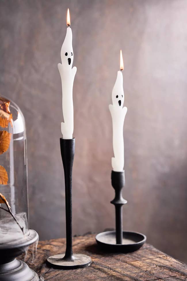Two ghost-shaped achromatic  candles with spooky faces are lit, placed successful  acheronian  candle holders, creating a Halloween-themed ambiance