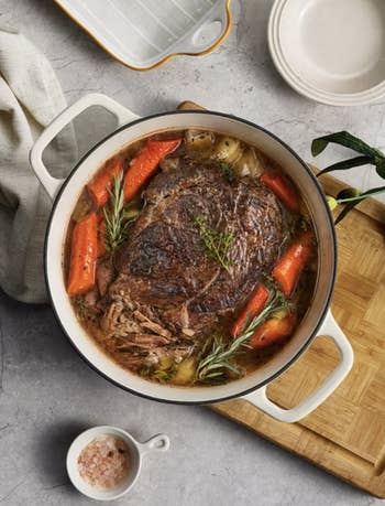 A cookware roast with carrots and herbs successful a achromatic casserole dish, placed connected a woody board, with plates and a cloth nearby
