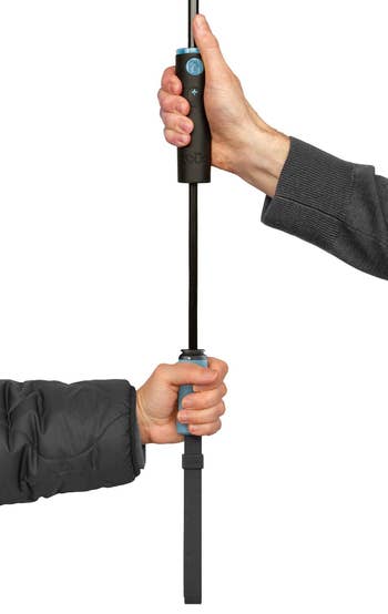 a pair of hands holding the umbrella at two different points on the extended handle 