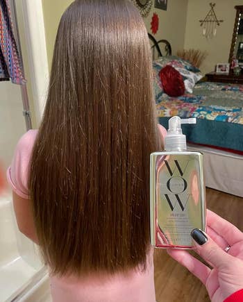 Person holding a hair care product beside long, straight hair, likely endorsing its use