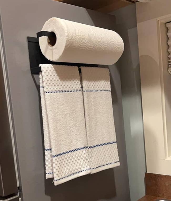 Large paper towel roll mounted above a smaller towel hanging on a bar magnetized to a fridge 
