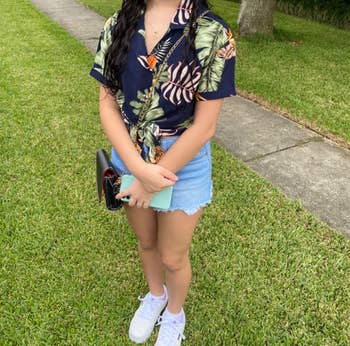 Person successful  a tropical people     garment  and denim skirt stands connected  grass, holding a clutch and phone. Wearing achromatic  sneakers