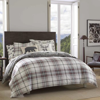 Reviewer image of gray, black, and white plaid comforter and matching shams with a bear throw pillow and deer throw pillow on top of brown carpet