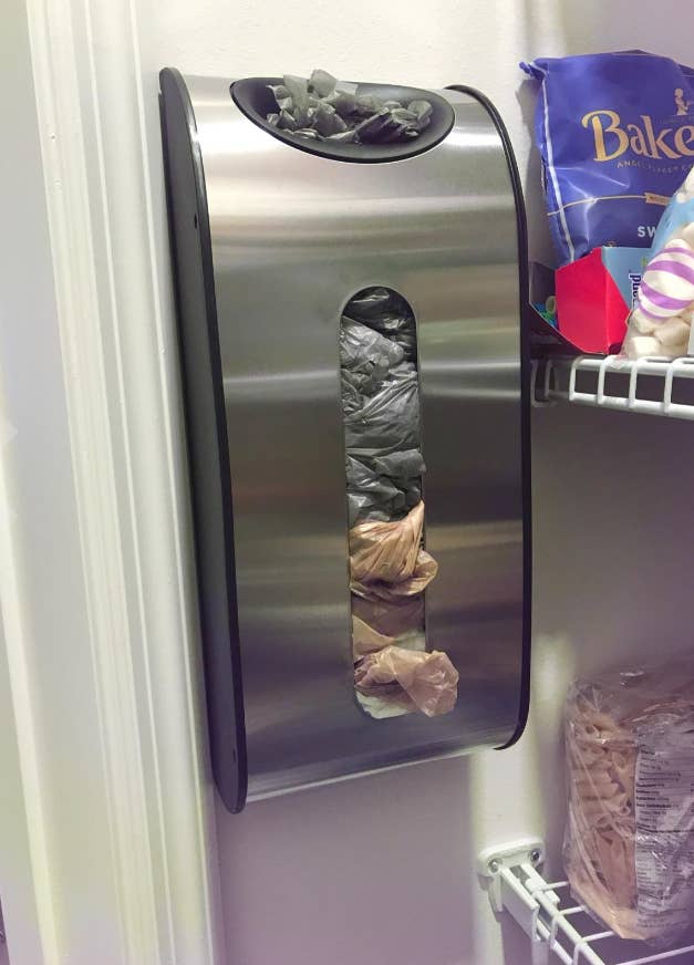 reviewer's grocery bag dispenser mounted to the wall with plastic bags in it