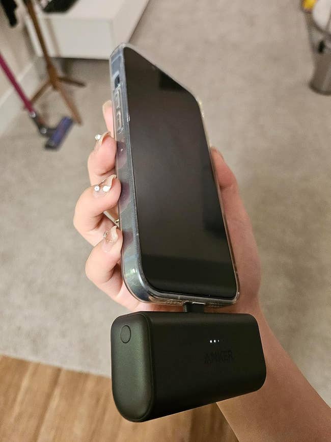 Hand holding a smartphone attached to a portable Anker battery pack