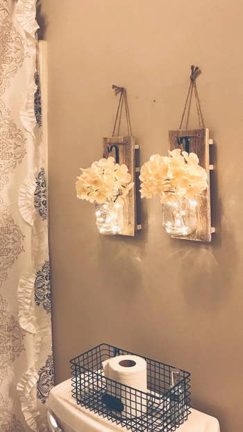 reviewer photo of the two mason jar wall sconces lit up and hanging in their bathroom