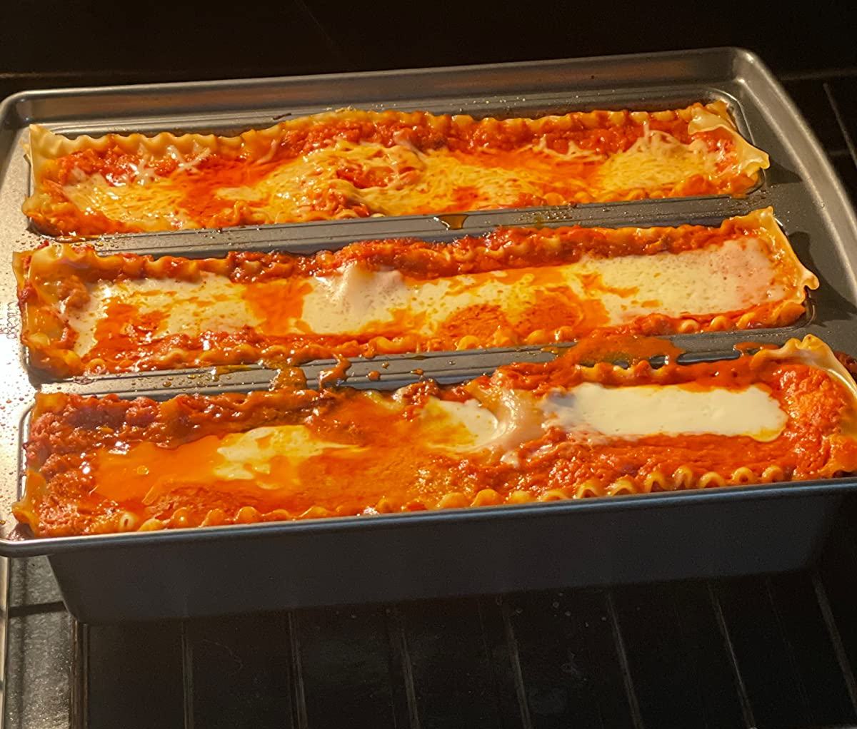 reviewer photo of the lasagna trio pan being used to bake three rows of lasagna in an oven