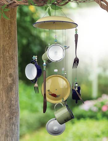 Wind chime made of repurposed kitchen utensils hanging from a tree in a garden