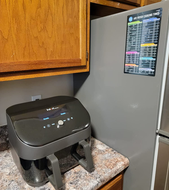 reviewer photo of the cheat sheet on the side of a fridge above an air fryer