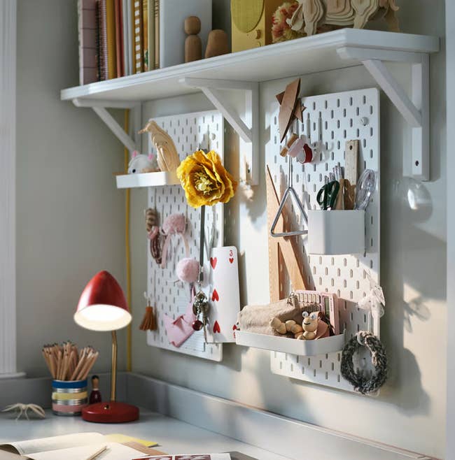 Organized workspace with a pegboard connected  a wall, featuring assorted  stationary items, decorative pieces, and a tiny  reddish  table  lamp