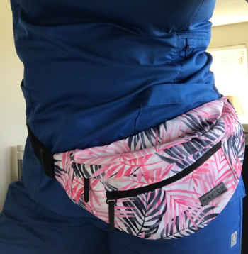 Bottom half of reviewer wearing navy blue, pink, and white plant patterned fanny pack around waist