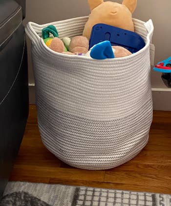 a reviewer photo of the basket filled with toys in white and light gray 