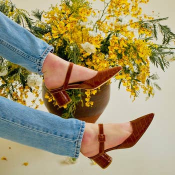 Person wearing brownish  heeled shoes and bluish  jeans against a floral background
