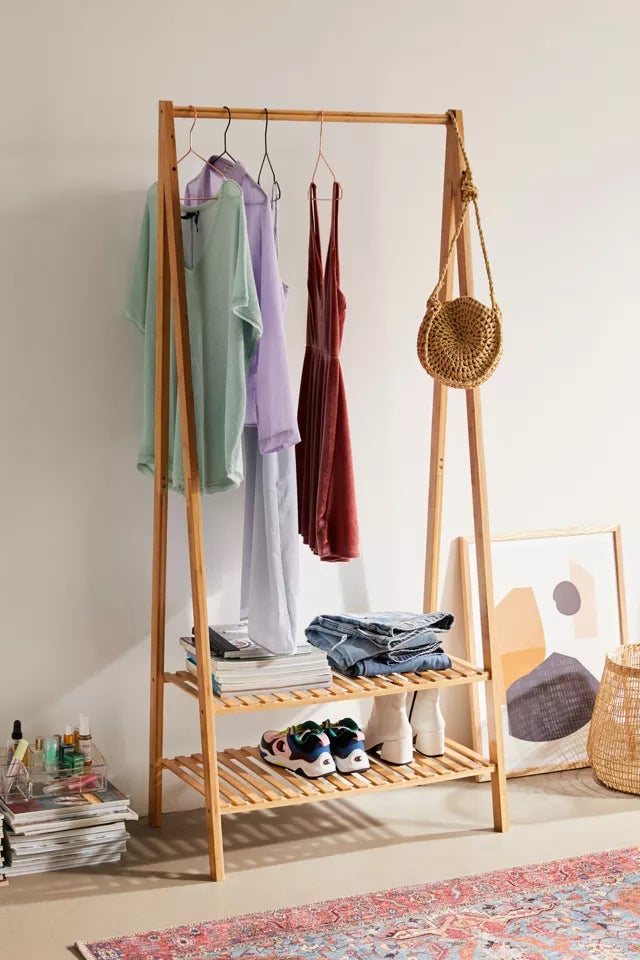 the wooden rack with clothes hanging on it and shoes on the shelf
