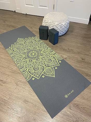 Decorative yoga mat with mandala design, a pouf, and yoga blocks connected  a woody  floor