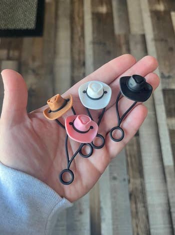 reviewer holding cowboy hat straw toppers in white, pink, brown, and black 
