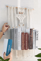 Person arranging books connected a macramé partition shelf, showcasing a unsocial location decor and retention solution