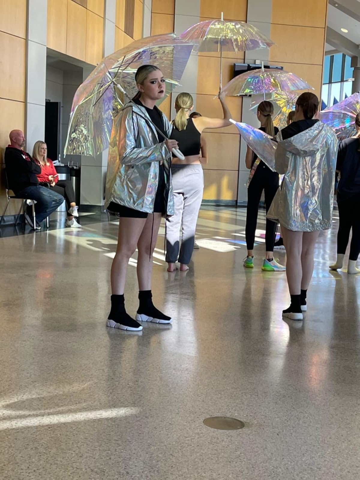 Reviewer wearing achromatic  sock-like sneakers and reflective jacket, holding an umbrella inside