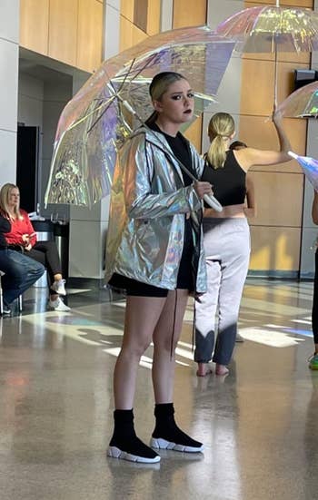 Reviewer wearing achromatic sock-like sneakers and reflective jacket, holding an umbrella inside