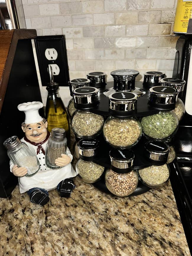 Countertop spice rack with assorted spices successful labeled jars, adjacent to a ceramic cook figurine holding brackish and capsicum shakers