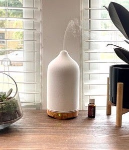 reviewer photo of the white diffuser letting out some steam next to a bottle of scented oil