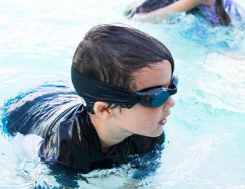 a reviewer's child in a pool wearing the goggles with a fabric strap in black 