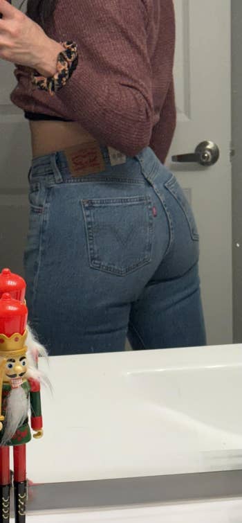 Person successful  a reddish  apical  wearing bluish  jeans stands by a mirror.