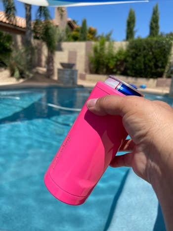 A manus holds a pinkish insulated tin cooler by a poolside, suggesting a refreshing portion successful a relaxed, sunny setting