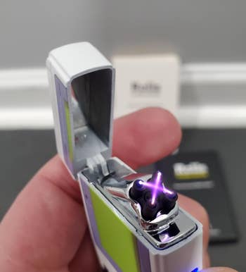 Hand holding an open lighter with an electrical plasma arc between electrodes