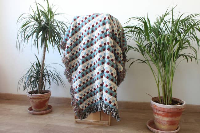 A throw blanket with a checkered pattern draped over a tall stool