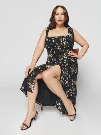 Model in black and white floral dress with a high leg slit seated
