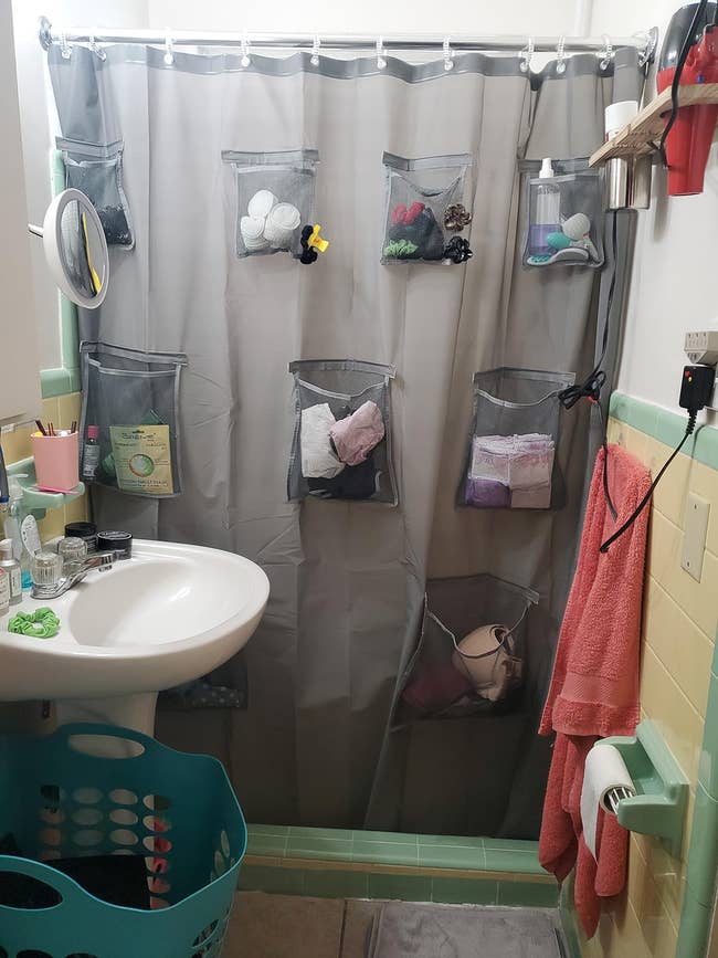grey Shower curtain with multiple pockets filled with bathroom items, providing a storage solution for small spaces
