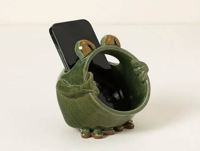 Green ceramic frog telephone holder with an open-mouth plan holding a smartphone upright