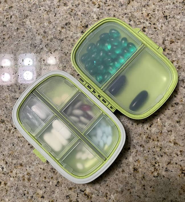 green travel pill case with eight different compartments filled with vitamins and medications